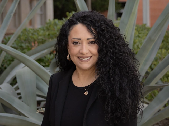 Cathleen Murphy smiles warmly in a headshot taken outdoors in front of large agave plants. She wears a black blazer and top, accessorized with gold earrings and a leopard print belt.